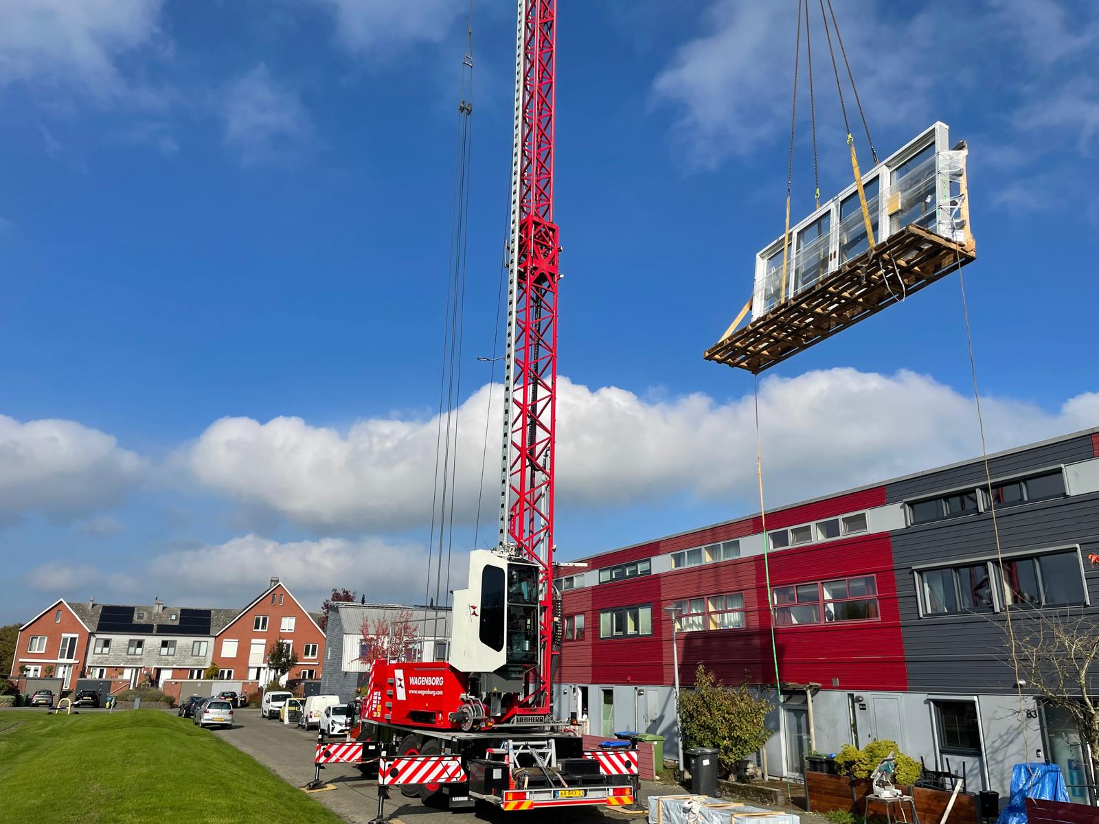 Kraan hijst een groot kozijnelement omhoog bij een appartementencomplex