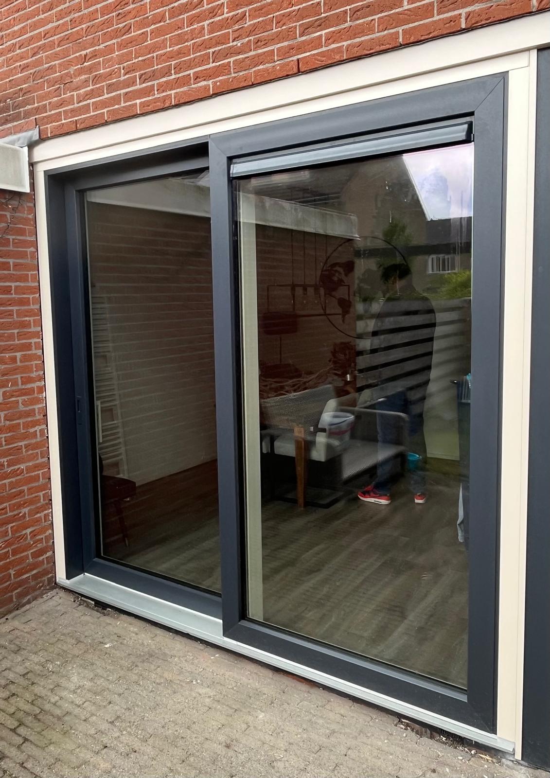 Antraciet aluminium schuifpui in een bakstenen gevel
